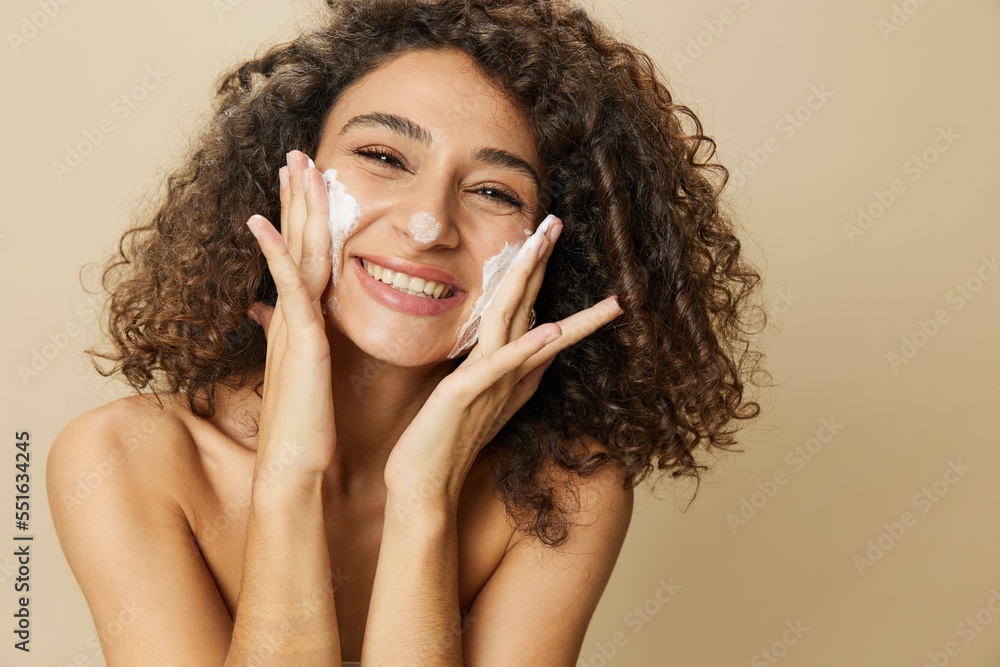 Woman beauty face close-up applying foam to wash and cleanse skin with fingers of her hand, nail and hair health, hair dryer style curly afro hair, body and beauty care concept
