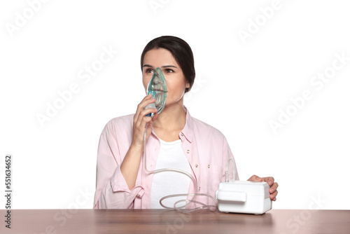 Young woman using nebulizer at wooden table on white background