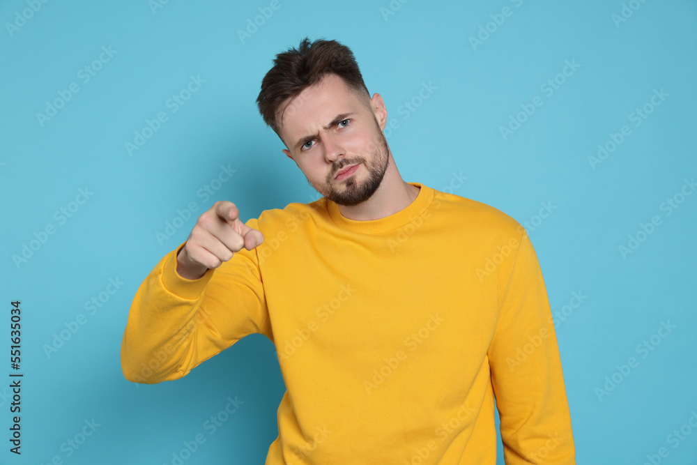 Aggressive man in yellow sweatshirt pointing at something on light blue background Aggressive man in yellow sweatshirt pointing at something on light blue background
