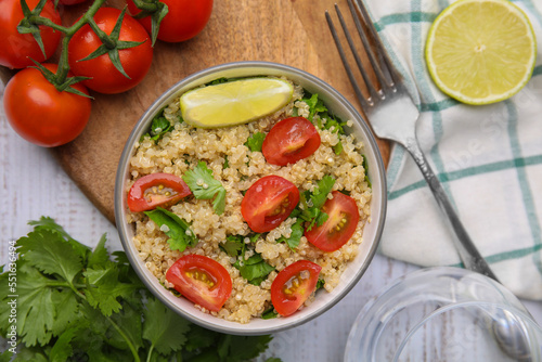 Delicious quinoa salad with tomatoes, parsley and lime served on white wooden table, flat lay