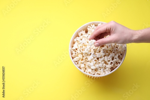 Woman taking delicious popcorn from paper bucket on yellow background, top view. Space for text