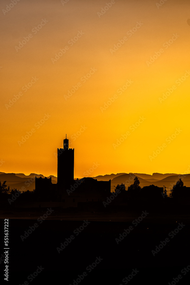 Silhouette of a typical Arab village with a mosque minaret at sunset. Ksar Tanamouste, Sahara, Morocco.
