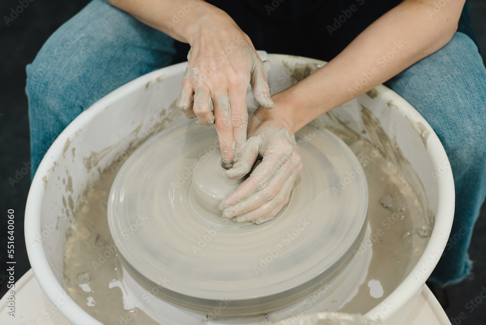 Closeup of potter hands working on pottery wheel in ceramic studio with clay hands front top view with pottery wheel in motion Closeup of potter hands working on pottery wheel in ceramic studio with clay hands front top view with pottery wheel in motion
