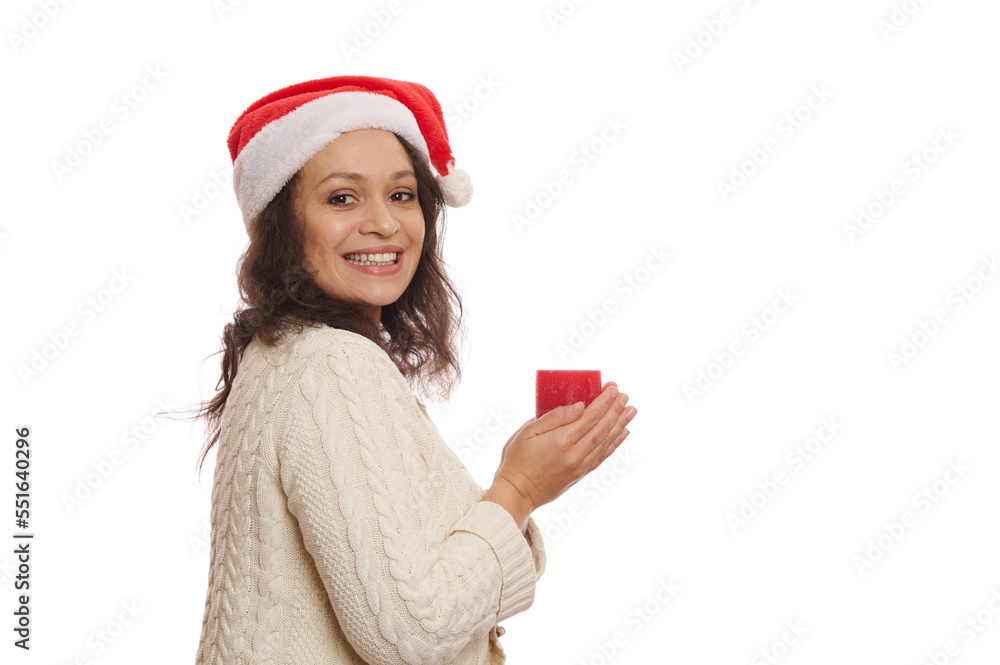 Side portrait of a charming woman in Santa hat, with Christmas candle, smiling a toothy smile while looking at camera through her shoulder, isolated on white background with copy advertising space Side portrait of a charming woman in Santa hat, with Christmas candle, smiling a toothy smile while looking at camera through her shoulder, isolated on white background with copy advertising space