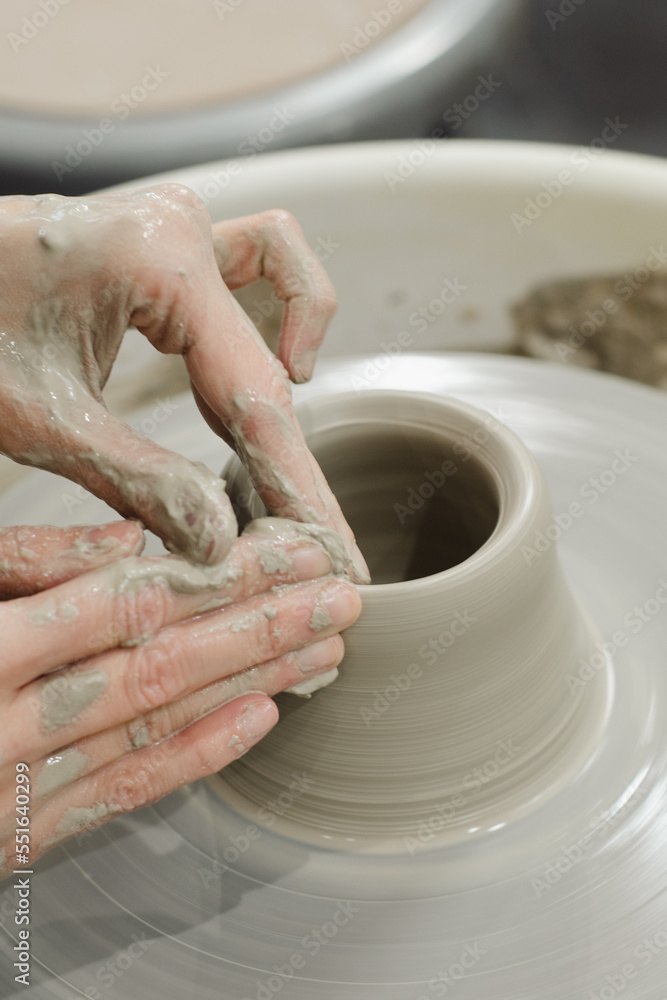 Closeup of potter hands working on pottery wheel in ceramic studio with clay hands top side view
