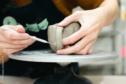 Hands of a potter attaching handle to pinch pot cup in ceramic studio pottery workshop using tools