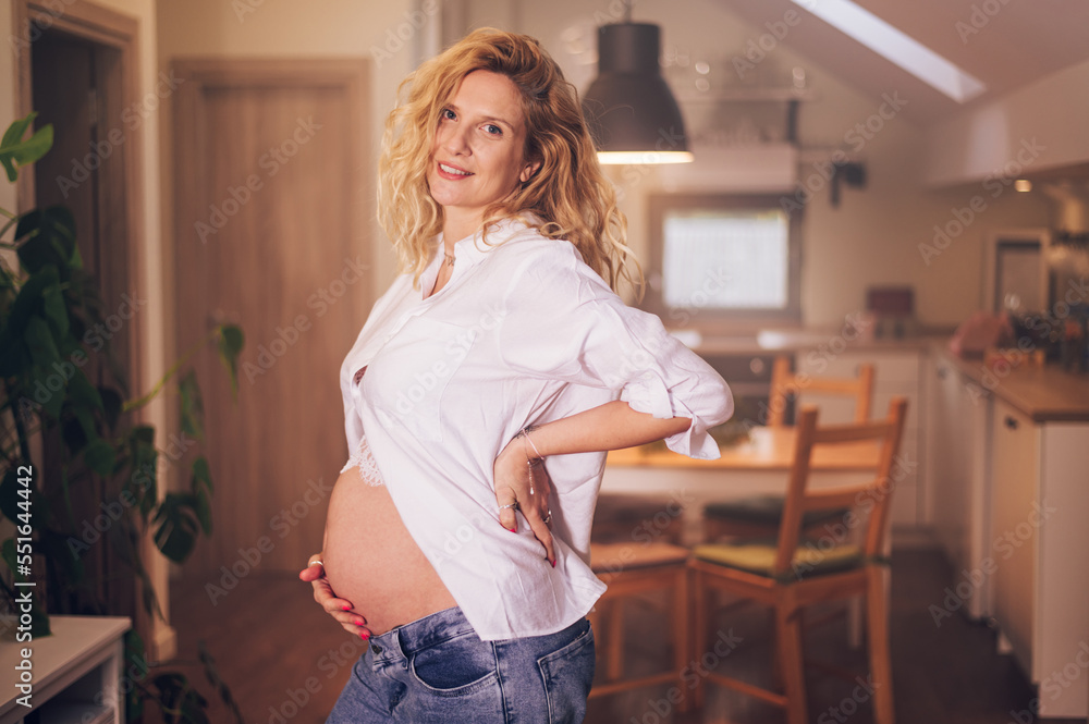 Portrait of pregnant woman standing at home holding hands on her belly Portrait of pregnant woman standing at home holding hands on her belly