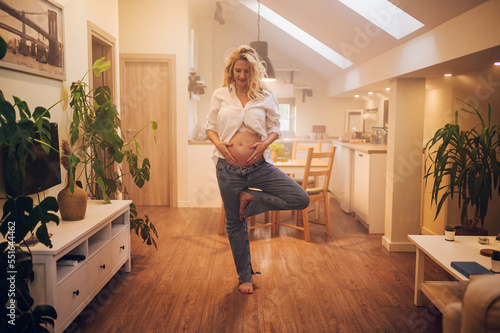 Portrait of pregnant woman standing at home holding hands on her belly