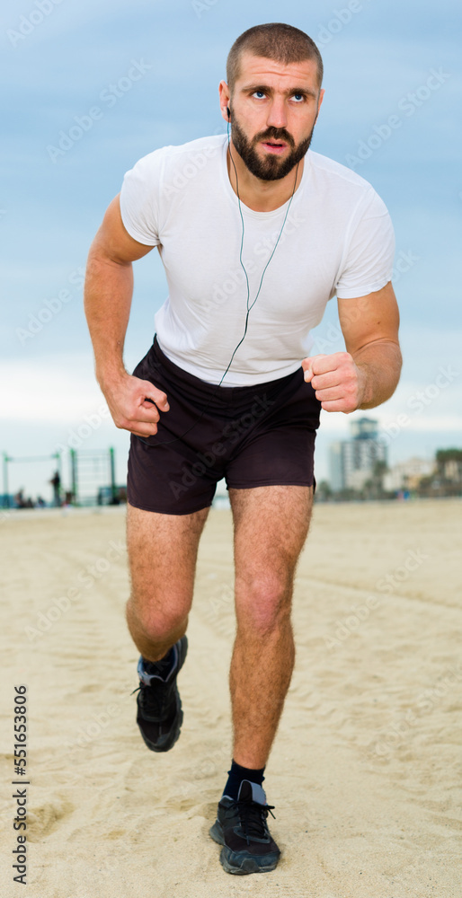 Athletic male in a white t-shirt running along the sidewalk in the city