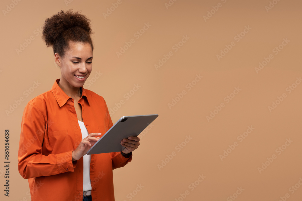 Young smiling African American woman using digital tablet isolated on beige background, copy space. Happy successful female shopping online. Technology concept Young smiling African American woman using digital tablet isolated on beige background, copy space. Happy successful female shopping online. Technology concept
