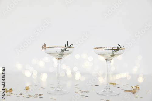 Two drinking glasses with champagne, bubbly wine. White table. Golden star shape confetti. Blurred background with bokeh lights. Festive still life. Birhday, anniversary party or celebration concept.