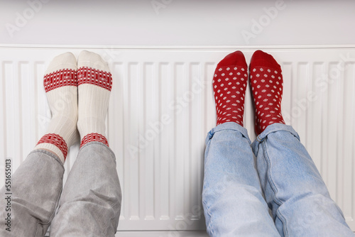 People warming feet near heating radiator, closeup