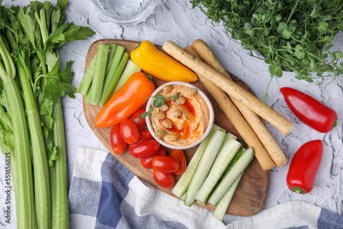 Board with delicious hummus, grissini sticks and fresh vegetables on light grey textured table, flat lay photo