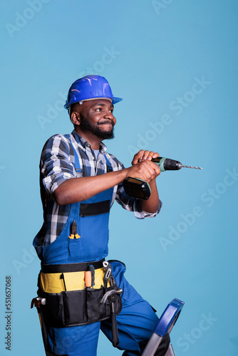 African american contractor drilling nails with electric power drill, working with electric machine on construction building. Professional man wearing hardhat with overalls to do renovation.