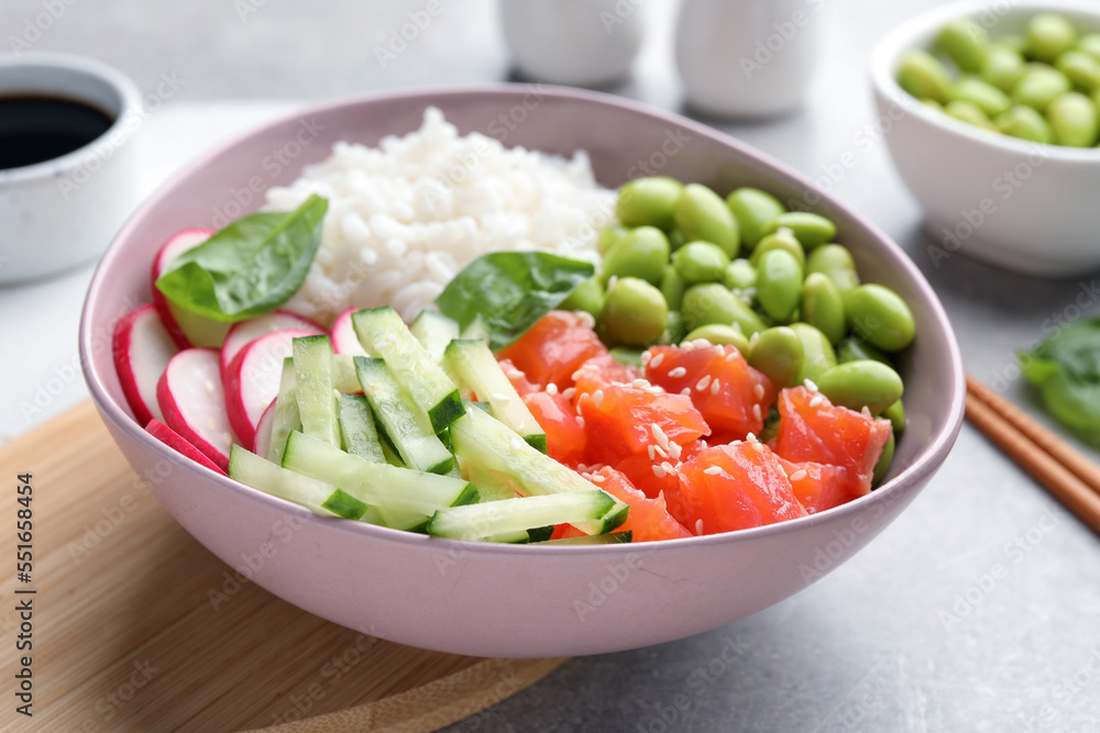 Poke bowl with salmon, edamame beans and vegetables on light grey table Poke bowl with salmon, edamame beans and vegetables on light grey table
