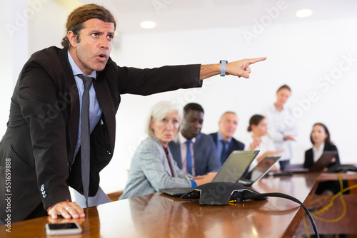 Portrait of furious mature white dark-haired male executive manager being angry with one of his subordinate employees and forcing him out during  photo