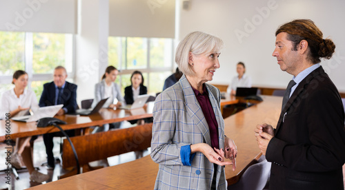 Businessman having conversation with senior woman manager in meeting room. Colleagues talking in company office.