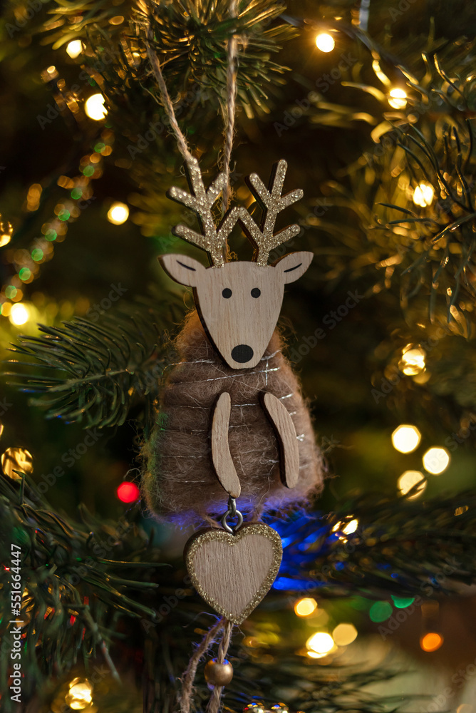 Christmas wooden deer, handmade, on the background of a Christmas tree decorated with lights of garlands