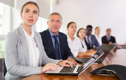Motivated young white blond female office worker in elegant suit sitting with colleagues in conference room 