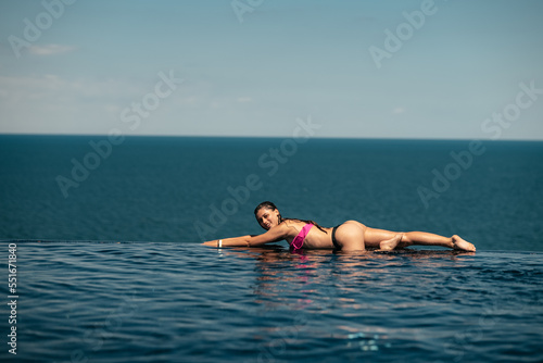 Happy woman in swimsuit swimming in infinity pool against seafront.
