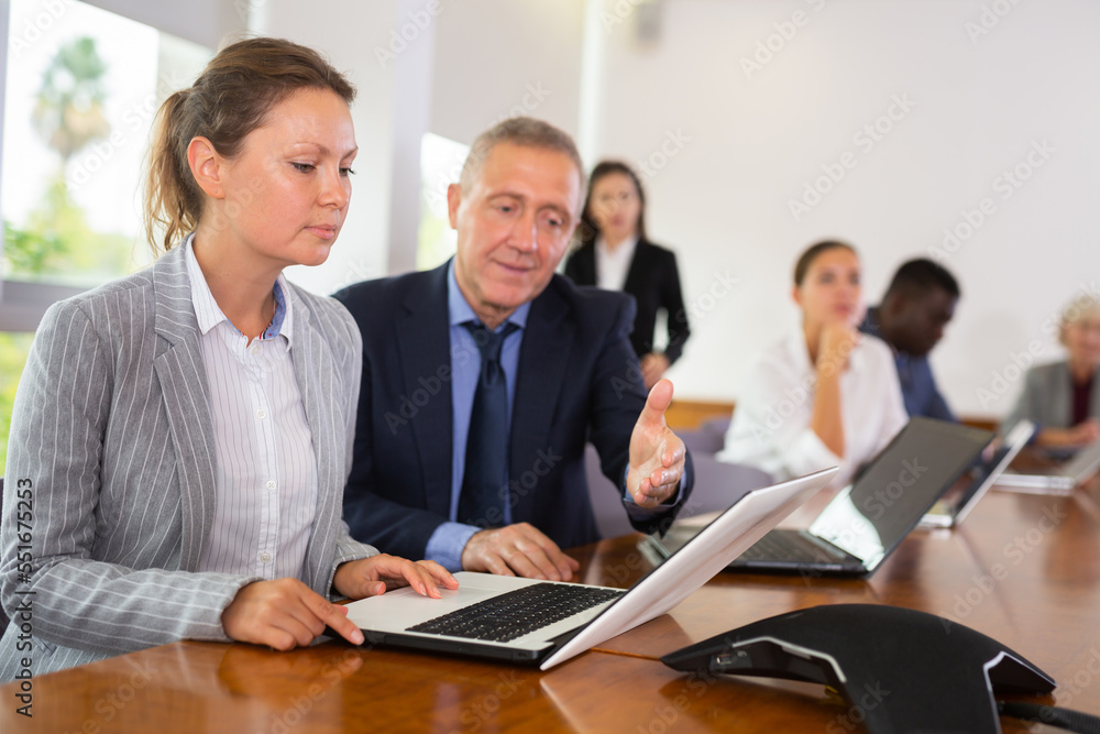 Obraz premium Woman secretary using laptop and discussing job with her employer, middle aged man, during meeting in conference room.