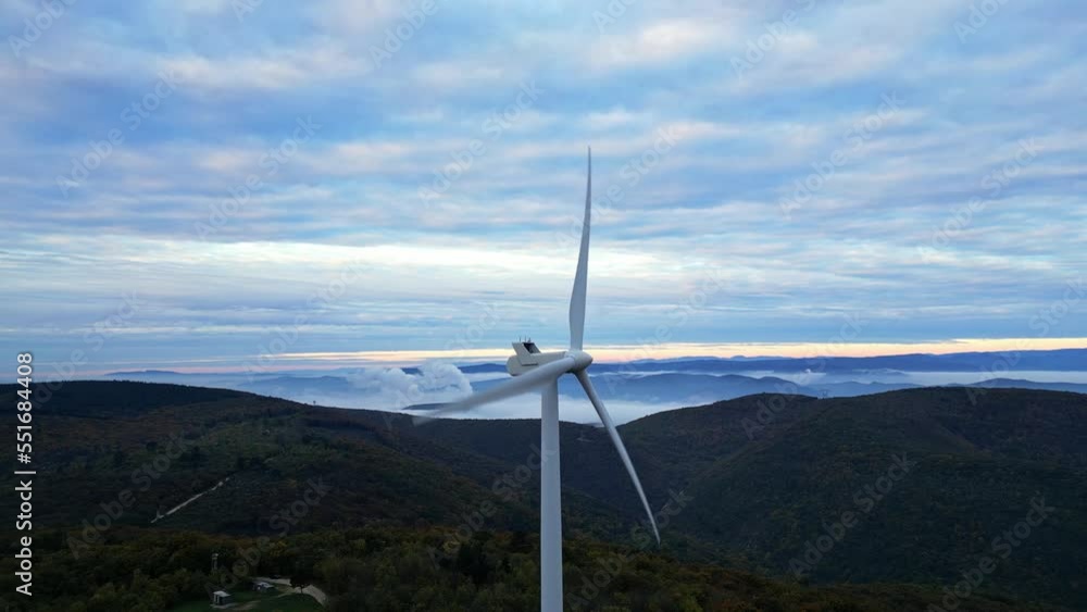 Wind turbines in the mountains during sunrise and thick morning fog in the valley. Wind farm producing green energy. Wind turbines in the mountains during sunrise and thick morning fog in the valley. Wind farm producing green energy.