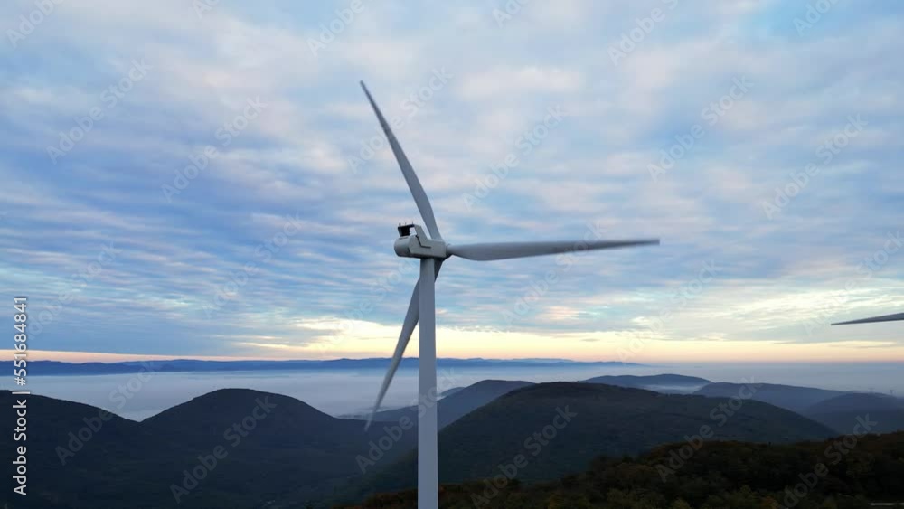 Wind turbines in the mountains during sunrise and thick morning fog in the valley. Wind farm producing green energy. Wind turbines in the mountains during sunrise and thick morning fog in the valley. Wind farm producing green energy.