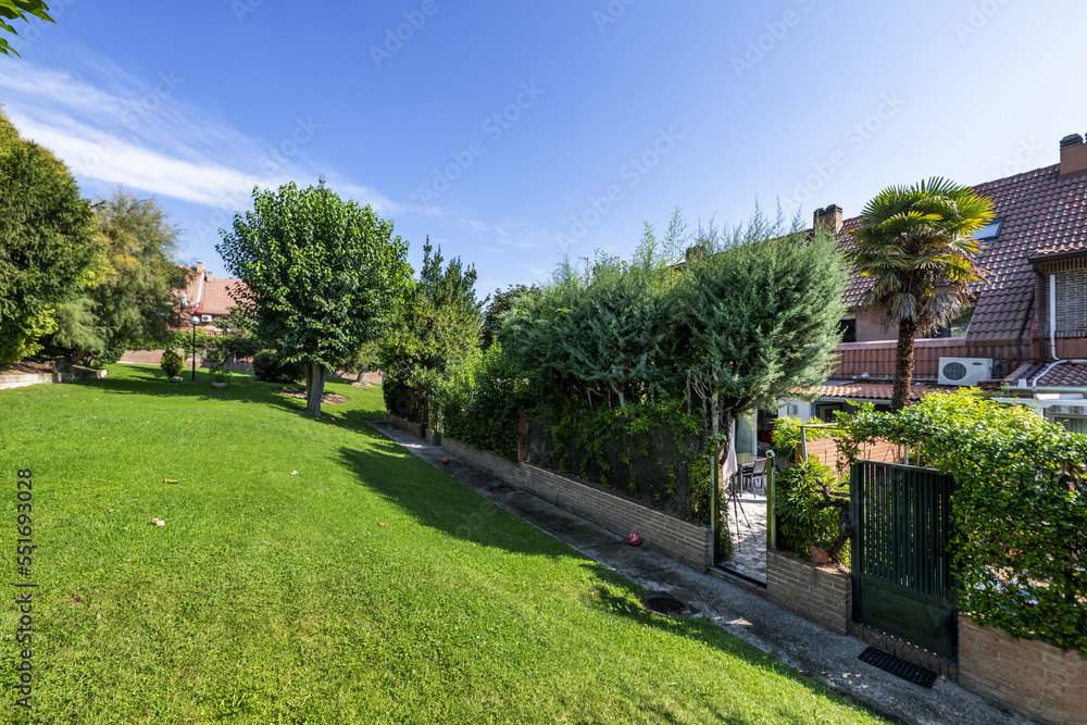 Facades of semi-detached single-family residential homes in an urbanization with common areas full of grass and leafy trees