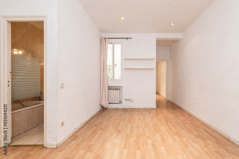 Fototapeta premium Empty living room with access to a bathroom and a small window with curtains to an interior patio