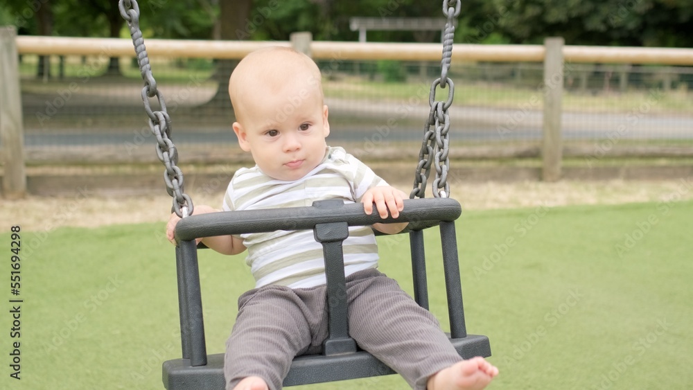 Funny Little Younger Newborn Infant Brother Boy On Swing. Baby Playing On Playground. Summer time outside. Kids Entertainment, Childhood, Child Development, Happy Family Concept