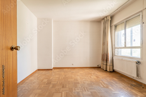 Empty room with checkerboard parquet flooring and window with old curtains