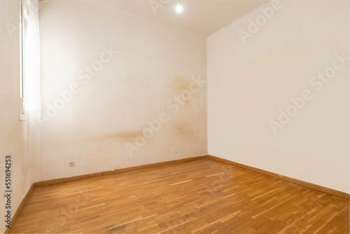 An empty room with walls in need of a lick of paint and worn laminated flooring