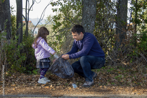 Father and daughter in the woods collecting plastic bottles. Cleaning and recycling of nature. Safeguarding the planet. 