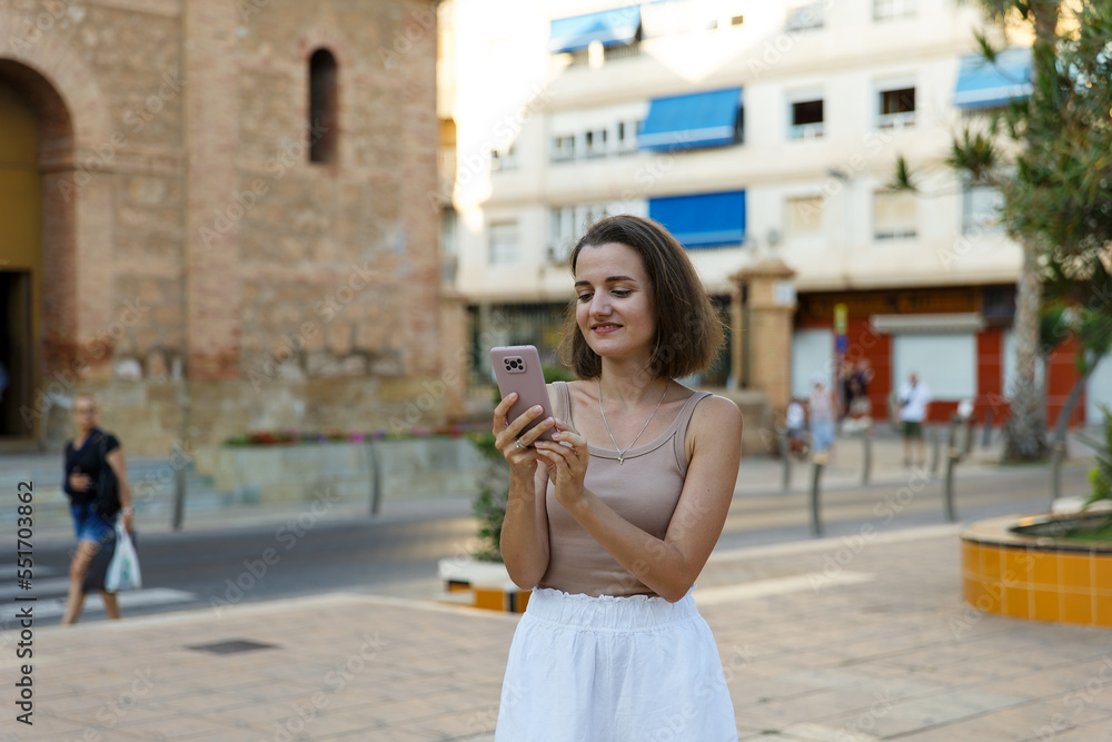 A young stylish woman communicates on a smartphone on a city street