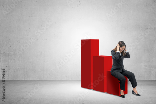 Asian businesswoman sitting on decreasing graph with frustrated expression