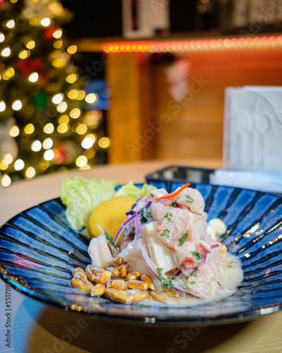Peruvian ceviche served on a blue plate, with Christmas lights in the background
