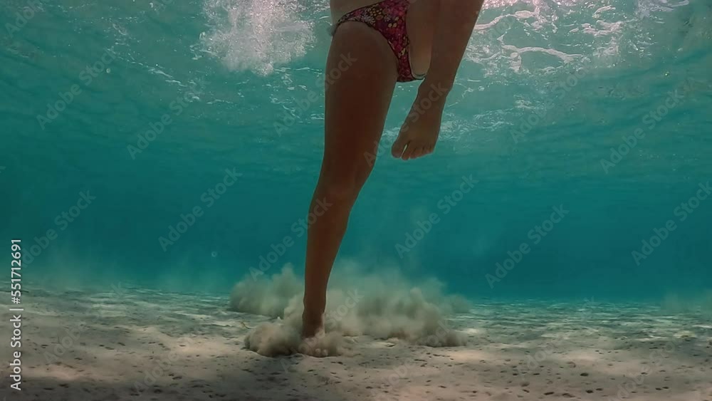Underwater scene of little girl jumps on seabed raising clouds of sand in transparent water. Super slow motion low angle point of view