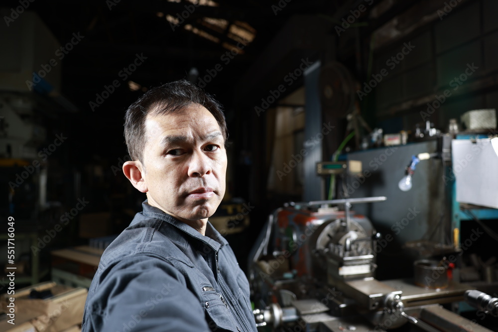 Metalworker in gray work clothes and a lathe in a small to medium-sized small business town factory. Conceptual images of the essence of manufacturing and technical succession. Metalworker in gray work clothes and a lathe in a small to medium-sized small business town factory. Conceptual images of the essence of manufacturing and technical succession.