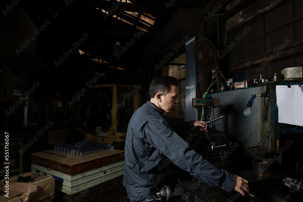 Metalworker in gray work clothes and a lathe in a small to medium-sized small business town factory. Conceptual images of the essence of manufacturing and technical succession.