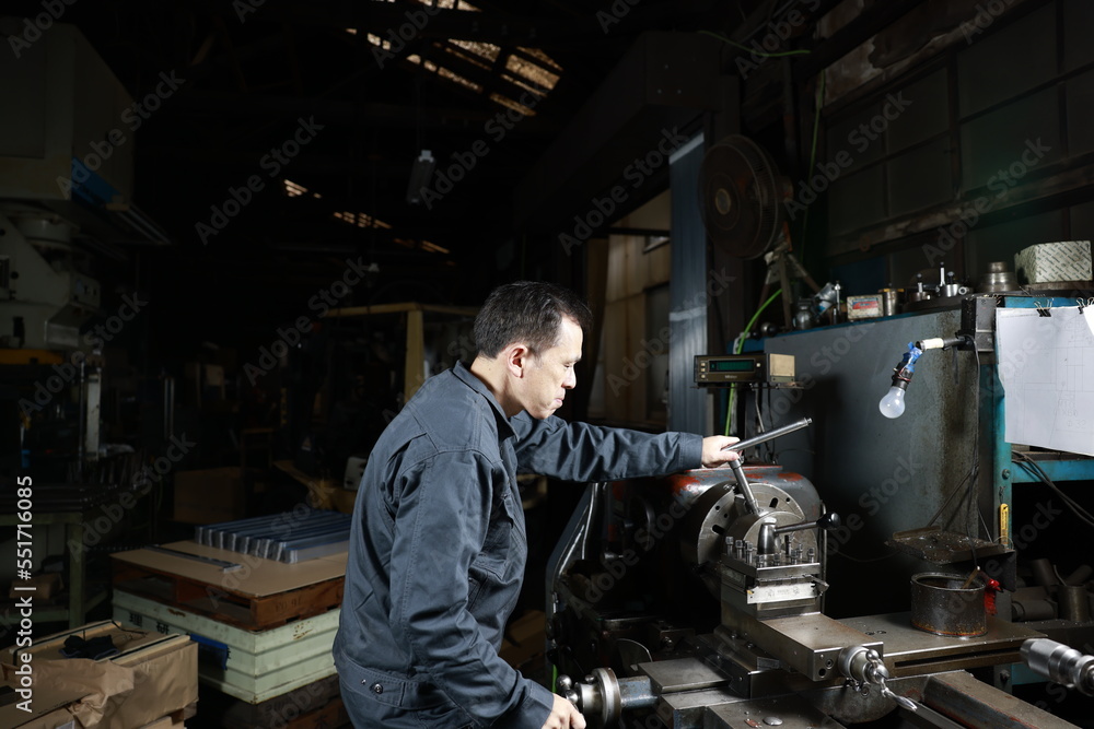 Metalworker in gray work clothes and a lathe in a small to medium-sized small business town factory. Conceptual images of the essence of manufacturing and technical succession. Metalworker in gray work clothes and a lathe in a small to medium-sized small business town factory. Conceptual images of the essence of manufacturing and technical succession.