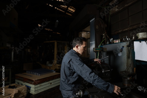 Metalworker in gray work clothes and a lathe in a small to medium-sized small business town factory. Conceptual images of the essence of manufacturing and technical succession.