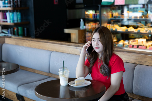 A woman talking on phone with friend while eating cake and drink in restaurant