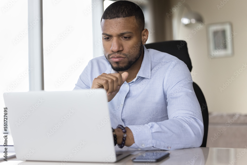 Serious focused young African business man using Internet app on laptop at office workplace, reading email letter, watching online presentation, business communication technology Serious focused young African business man using Internet app on laptop at office workplace, reading email letter, watching online presentation, business communication technology