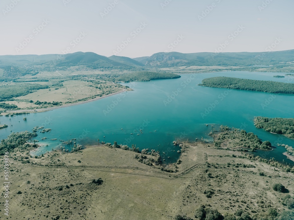 Obraz premium Aerial view on mountain lake. Drone over water reservoir at mountain valley covered with green spring forest. Beautiful view from above on smooth blue surface of mountain lake among highlands. Nobody