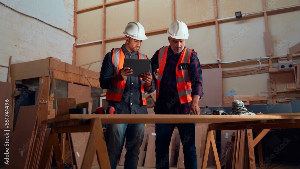 Men in safety helmet looking at digital tablet next to power tools in woodworking factory Men in safety helmet looking at digital tablet next to power tools in woodworking factory