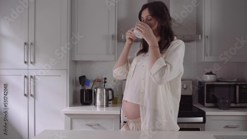 Pregnant woman drinking coffee. Caucasian girl enjoys her morning cup of coffee on her kitchen. Pregnancy and caffeine.