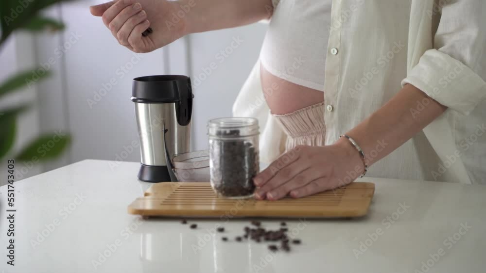 Pregnant woman making coffee. Close up of Caucasian woman's belly with coffee beans and cup on kitchen table. Pregnancy and caffeine. Pregnant woman making coffee. Close up of Caucasian woman's belly with coffee beans and cup on kitchen table. Pregnancy and caffeine.