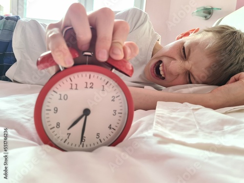 Foto Stressed tired boy sleeping in bed with an alarm clock