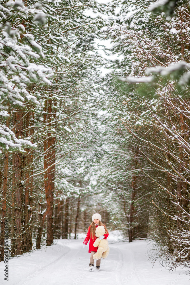 girl with a big stuffed bear toy walks in the winter forest