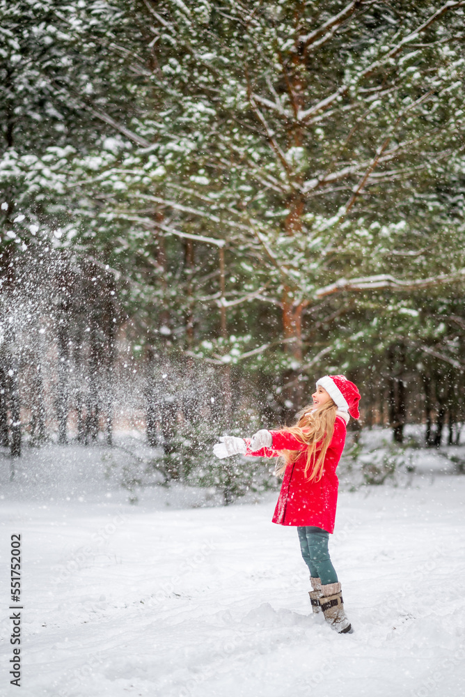girl in a red coat throws snow in a winter forest